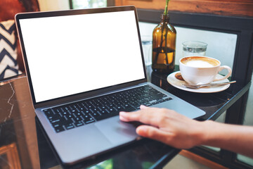 Mockup image of a hand touching on laptop computer touchpad with blank white desktop screen on the table