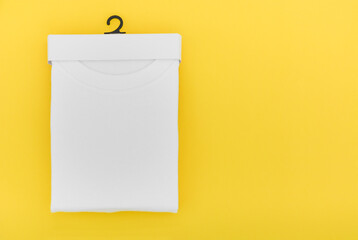 Wall Mural - top view of folded white color t-shirt in paper hanging package on yellow background, copy space, flat lay