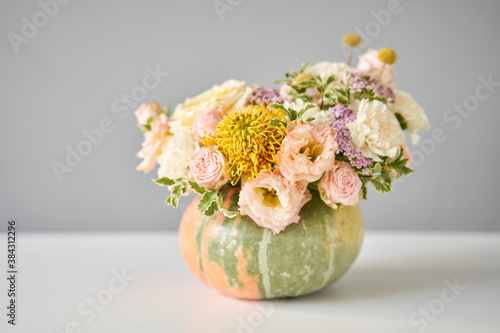Flowers arrangement in pumpkin on the white table. Fresh cut flowers for decoration home. European floral shop. Delivery fresh cut flower.
