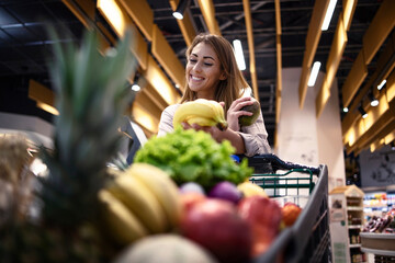 Grocery shopping. Female person holding fruits in supermarket and smiling. Buying healthy food at supermarket.