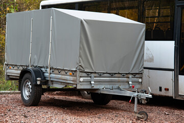 A car trailer covered with a gray tarpaulin in an unpaved parking lot.