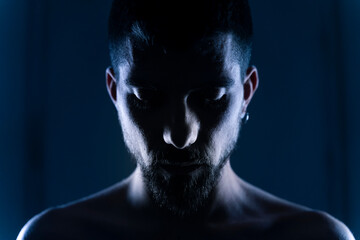 Handsome and strong man portrait posing with light of neon lamps and smoke over dramatic blue neon background in a dark room. 