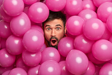 Close Up Shot Of Shocked Bearded European Man Looks With Widely Opened Mouth At Camera Being Greatly Surprised Poses Over Inflated Pink Balloons Impressed To Get Unexpected Gift On Birthday.