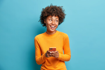 Wall Mural - carefree pleased female student uses mobile phone for online distant education looks gladfully aside