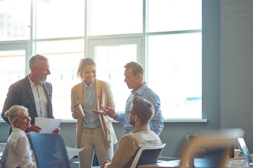 Wall Mural - Powerfully successful team. Group of multiracial business people in classic wear discussing work and sharing ideas while standing in the modern office or coorking space