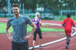 © TheSupporter - Young Caucasian man on athletic track, standing with hands on his hips, looking at camera
