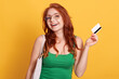 © sementsova321 - Portrait of woman holding shopping bag and credit card isolated over yellow background, red haired female being ready to do shopping, excited lady enjoying her purchases.