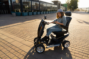 Wall Mural - Woman tourist with smartphone on a four wheel mobility electric scooter on a city street.