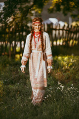 Wall Mural - A beautiful Slavic girl with long blonde hair and brown eyes in a white and red embroidered suit stands by a wooden fence.Traditional clothing of the Ukrainian region.