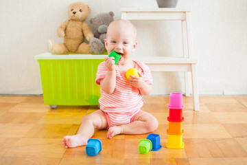 Little baby girl sitting on the floor, crawling and playing with brightly colored educational toys