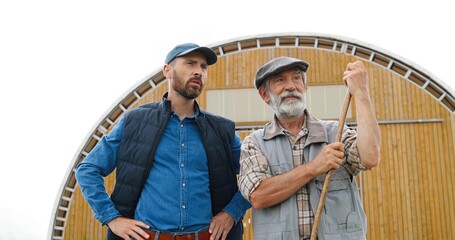 Wall Mural - Caucasian young man standing outdoor with old retired father in farm and talking, asking for advice. Males farmers speaking and discussing farming work. Countryside. Son and senior father.