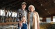 © VAKSMANV - Portrait of Caucasian cheerful mother, old grandmother and cute small pretty girl in stable with sheep smiling to camera. senior woman with daughter and granddaughter standing in barn with livestock.