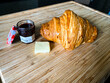 Croissant raspberry jam and pad of butter on bamboo wood cutting board