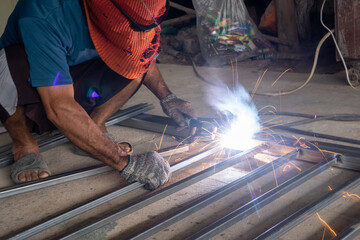 Wall Mural - The welder is welding the parts of the iron door. The person working on a welder using an electric welding machine.