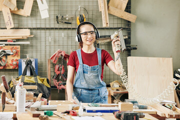 Portrait of pretty young Asian female carpenter in earmuffs and goggles working with upholstery staplers