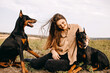 Young woman sitting on green grass with two doberman breed dogs.