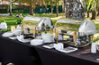 © EkaterinaKiseleva - Outdoor catering banquet in summer. Banquet table with chafing dish, plates and cutlery