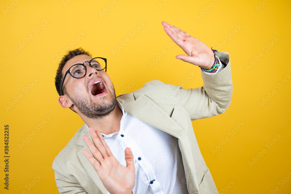 Scared Arm Young handsome businessman wearing suit over isolated yellow background ...