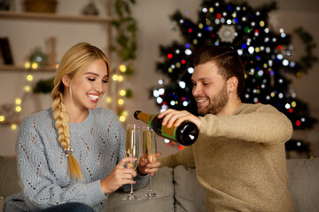 Wall Mural - Young couple drinking champagne, celebrating New Year together at home