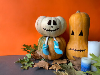 Cute Halloween wallpaper with white pumpkin with legs wearing blue socks, orange long pumpkin and candles against orange background