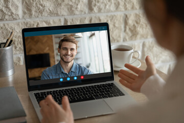 Close up back view of woman talk speak on video call on laptop with smiling male colleague coworker. Female employee have webcam digital virtual conference with partner. Online communication concept.