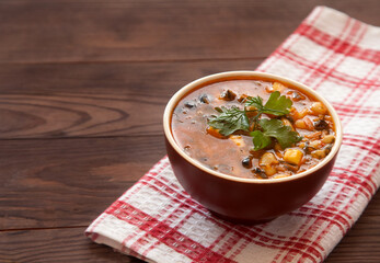 Wall Mural - Bean soup with olives and parsley stands on a linen red tablecloth on a wooden table. Copy spaes.