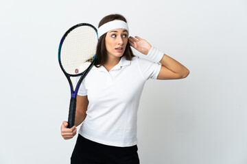 Young woman tennis player over isolated white background listening to something by putting hand on the ear