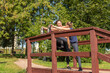 © Андрей Рыков - Mother and daughter stretching legs together on top of wooden staircase in public park on sunny summer morning. Family outdoor sports theme.