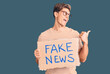 © Krakenimages.com - Young handsome man holding fake news banner pointing thumb up to the side smiling happy with open mouth