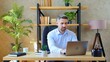 © viacheslav - Gray-haired smiling business man freelancer manager SEO sits on chair at table in home office works remote distance online uses laptop computer typing on keyboard