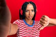 Beautiful hispanic woman taking a selfie photo wearing headphones with angry face, negative sign showing dislike with thumbs down, rejection concept