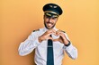 © Krakenimages.com - Handsome hispanic man wearing airplane pilot uniform smiling in love doing heart symbol shape with hands. romantic concept.