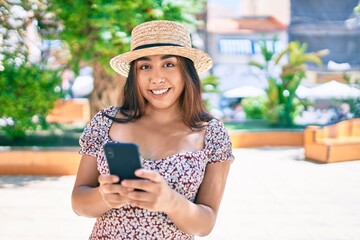 Young latin woman on vacation using smartphone walking at street of city.