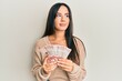 © Krakenimages.com - Young beautiful hispanic girl holding 10 colombian pesos banknotes smiling looking to the side and staring away thinking.