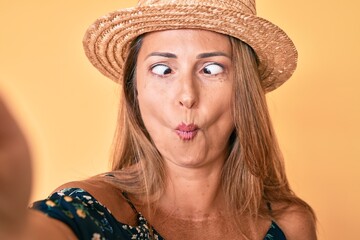 Canvas Print - Middle age hispanic woman wearing summer hat taking a selfie making fish face with mouth and squinting eyes, crazy and comical.