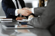 © Iryna - Unknown businessman shaking hands with his colleague or partner above the glass desk in modern office, close-up. Business people group at meeting