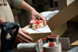 © insta_photos - Female online store small business owner seller holding free gift packing package post shipping box preparing delivery parcel on table. Commercial dropshipping holiday presents sale concept. Closeup.