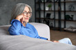 © insta_photos - Beautiful relaxed mature old woman relaxing sitting on couch at home. Peaceful middle aged grey-haired lady wearing glasses resting on sofa enjoying lounge, no stress, peace of mind, looking away.