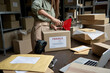 © insta_photos - Female post mail storage worker holding tape dispenser sealing shipping online store order courier delivery cardboard box packing ecommerce fragile dropshipping parcel in distribution warehouse.