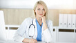 © Iryna - Woman-doctor at work while sitting at the desk in sunny clinic. Blonde cheerful physician filling up medication history record form