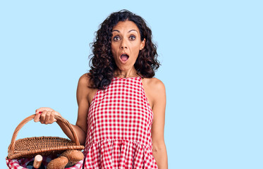 Sticker - Middle age beautiful woman holding picnic basket with food scared and amazed with open mouth for surprise, disbelief face