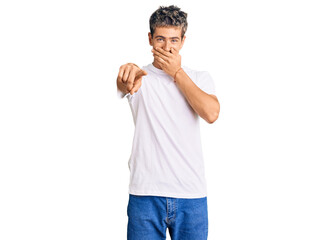 Wall Mural - Young handsome man wearing casual white tshirt laughing at you, pointing finger to the camera with hand over mouth, shame expression