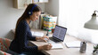 © fizkes - Side view focused young beautiful caucasian woman wearing wireless headphones, studying remotely using laptop at home office, smart millennial female student involved in research article writing.