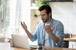 © fizkes - Frustrated angry young man in eyeglasses looking at laptop screen, feeling nervous about bad device work or poor internet connection in kitchen. Unhappy shocked guy reading message with bad news.