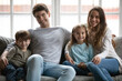© fizkes - Portrait of smiling young Caucasian family with two small kids sit relax on sofa in living room together. Happy parents rest on couch on weekend at home with little children, show love and care.