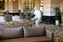 Professional Fully Armed Disinfector Against Covid-19 (coronavirüs, Pandemic) Using Sprays To Remove Bacteria From The Surface At The Hotel. Man Wearing A Protective Mask, Gloves And Suit.