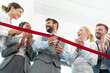 Businessman cutting red ribbon with colleagues at office