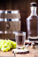 distilled drink based on fermented grapes, in a shot glass, rustic wood background with oak barrel