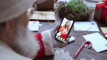 Wall Mural - Over shoulder view of Santa Claus video calling kid girl on mobile phone greeting child by webcam talk open Christmas gift box in virtual online chat meeting using smartphone sit at table on xmas.