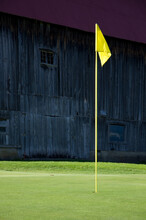 Yellow Golf Flag On Practice Green With Old Barn In Background